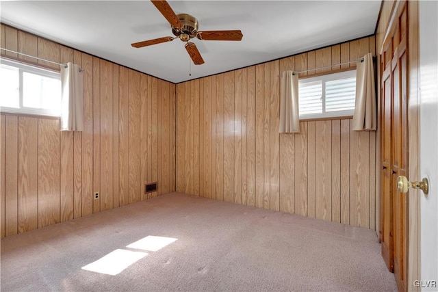 carpeted spare room featuring wooden walls, visible vents, and ceiling fan