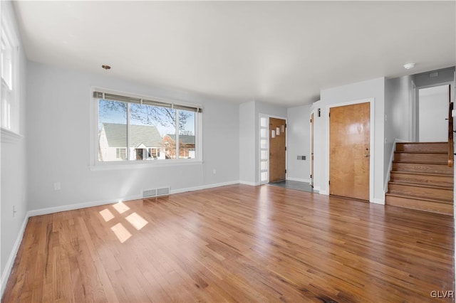 unfurnished living room featuring visible vents, baseboards, wood finished floors, and stairs