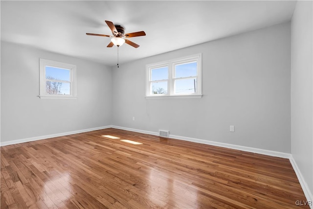 spare room with a wealth of natural light, visible vents, baseboards, and wood finished floors