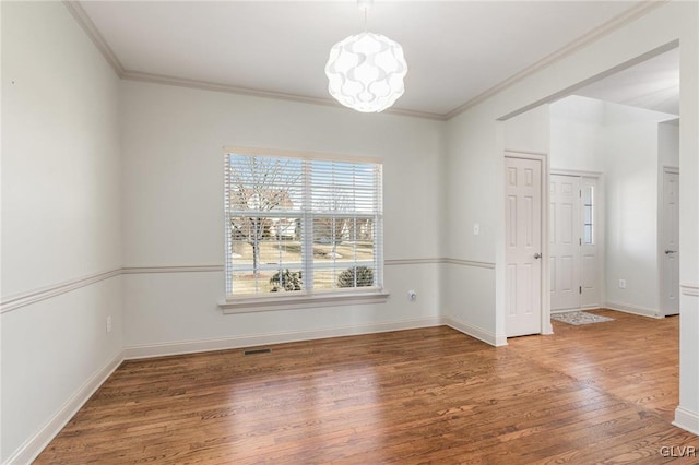 empty room featuring visible vents, ornamental molding, baseboards, and wood finished floors