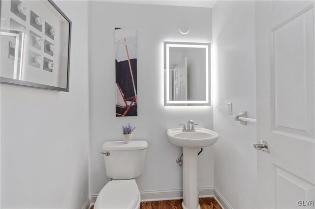 half bathroom with a sink, toilet, baseboards, and wood finished floors