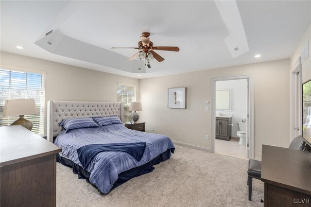 bedroom with baseboards, light colored carpet, a tray ceiling, recessed lighting, and ensuite bathroom