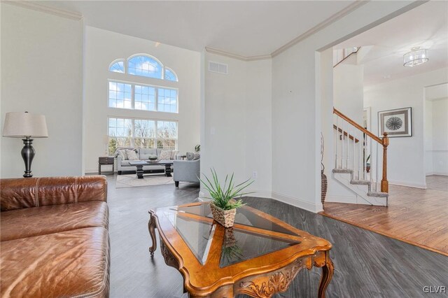 living room featuring wood finished floors, visible vents, baseboards, stairs, and crown molding