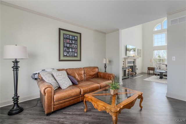 living area with baseboards, a lit fireplace, ornamental molding, and dark wood-style flooring