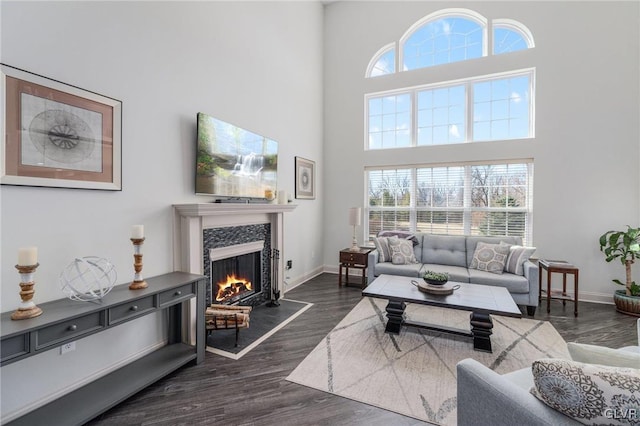 living area featuring dark wood finished floors, a towering ceiling, baseboards, and a warm lit fireplace