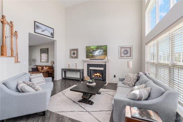 living area with a fireplace, wood finished floors, baseboards, and a towering ceiling