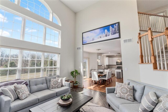 living area with visible vents, baseboards, wood finished floors, and stairway