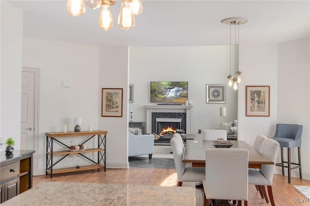 dining room featuring an inviting chandelier, wood finished floors, baseboards, and a warm lit fireplace