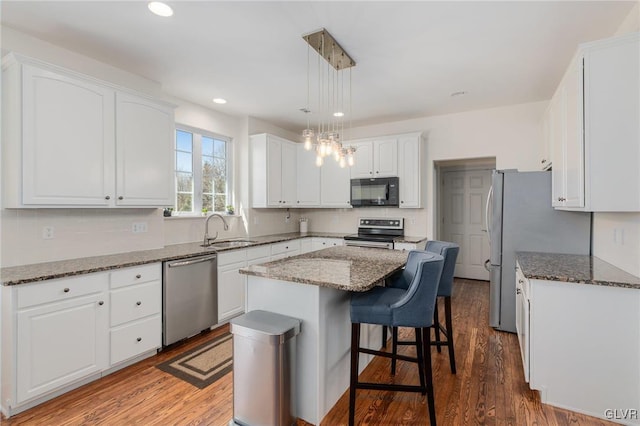 kitchen featuring wood finished floors, a kitchen island, a sink, stainless steel appliances, and white cabinets