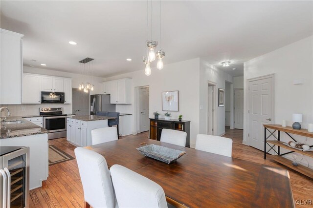 dining space with beverage cooler, light wood-style flooring, a notable chandelier, and recessed lighting