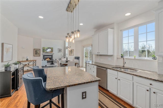 kitchen with a kitchen island, dishwasher, a lit fireplace, white cabinets, and a sink