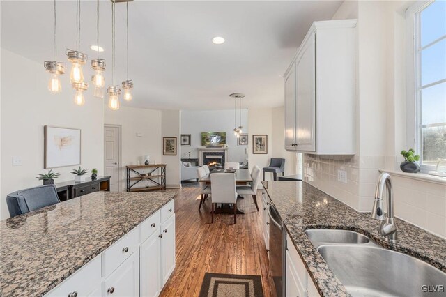 kitchen with tasteful backsplash, dishwasher, a warm lit fireplace, wood finished floors, and a sink