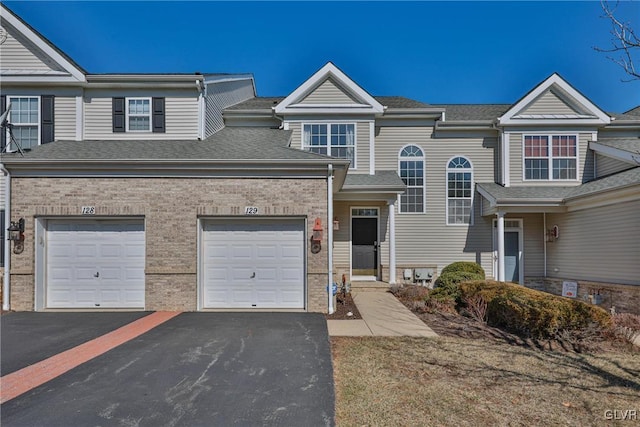 multi unit property with brick siding, driveway, and roof with shingles