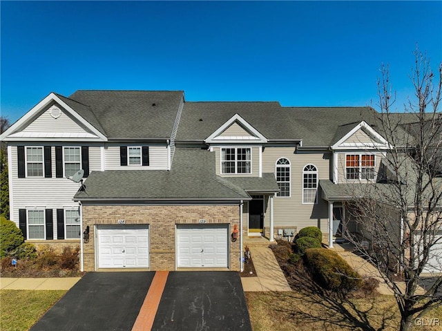 view of front of house featuring brick siding, driveway, and roof with shingles