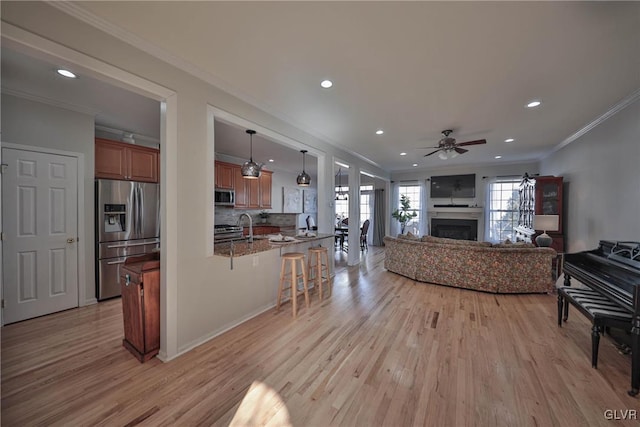 living room featuring light wood finished floors, a fireplace, crown molding, and a ceiling fan