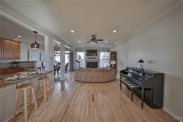 living area featuring a fireplace, light wood-type flooring, a ceiling fan, and ornamental molding