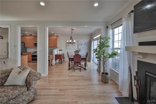 dining room featuring an inviting chandelier, recessed lighting, ornamental molding, light wood-style floors, and a glass covered fireplace