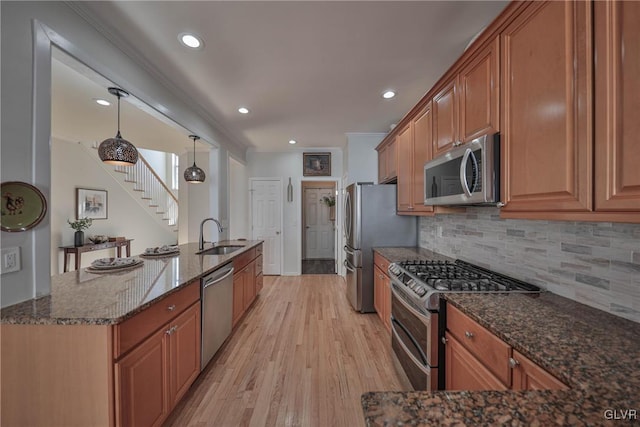 kitchen with tasteful backsplash, dark stone counters, light wood-style flooring, stainless steel appliances, and a sink