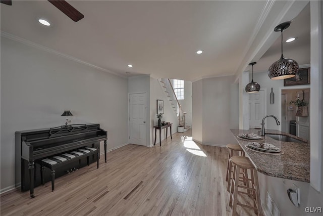 interior space with dark stone countertops, baseboards, light wood finished floors, ornamental molding, and a sink