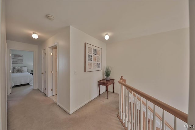 hall with an upstairs landing, light colored carpet, and baseboards