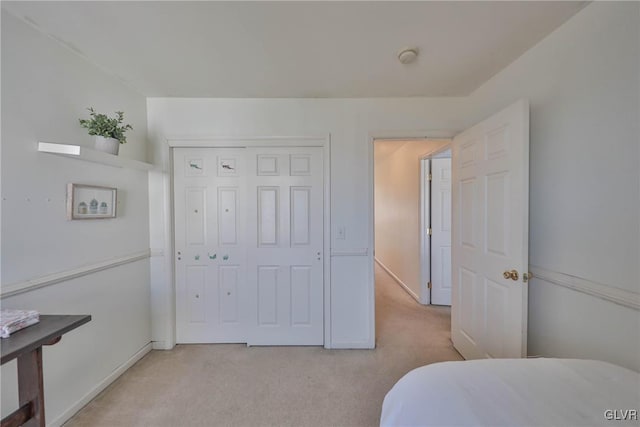 bedroom with a closet, light colored carpet, and baseboards