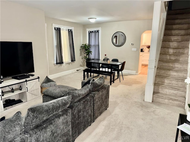 living room featuring stairway, light colored carpet, arched walkways, and baseboards