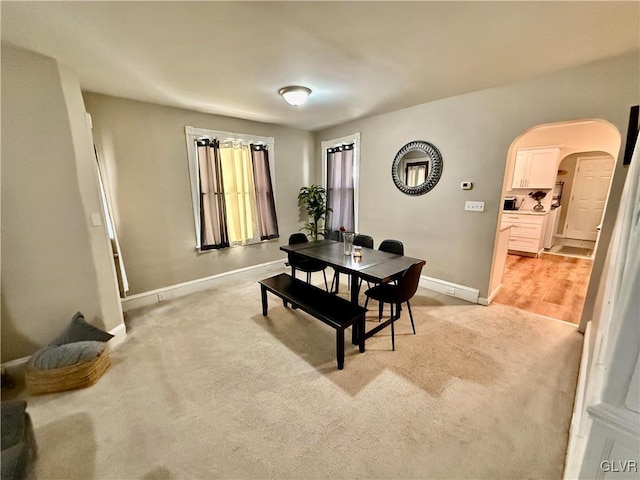 dining room with arched walkways, light carpet, and baseboards