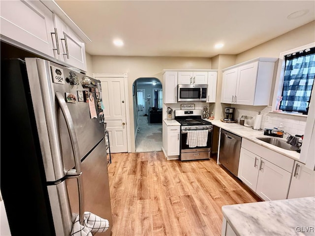 kitchen with arched walkways, stainless steel appliances, light countertops, and a sink