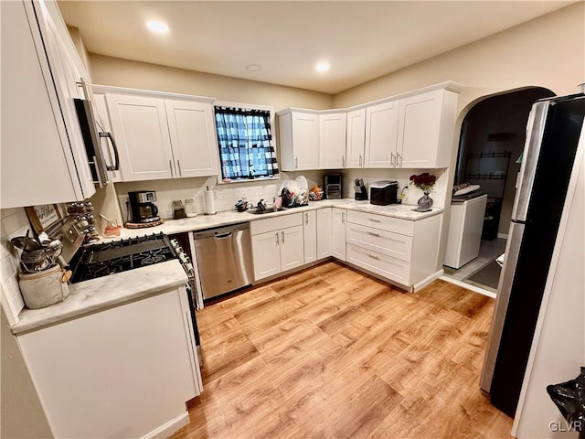 kitchen with tasteful backsplash, stainless steel appliances, light wood-style floors, arched walkways, and white cabinetry