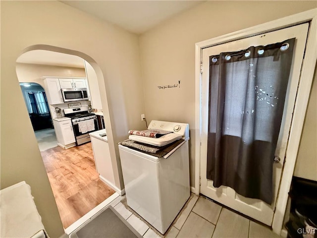 kitchen featuring washer / clothes dryer, arched walkways, light countertops, white cabinets, and appliances with stainless steel finishes