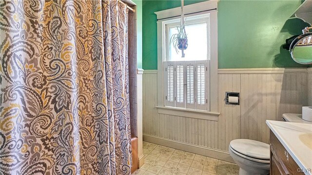 full bath with vanity, toilet, a wainscoted wall, and a wealth of natural light