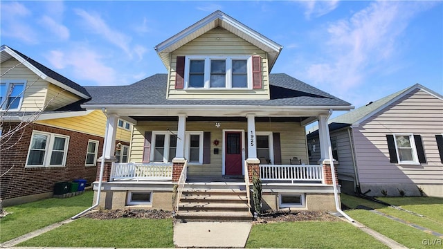 view of front of home with roof with shingles, a porch, and a front yard