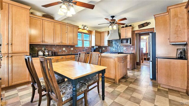 kitchen with light floors, a ceiling fan, custom exhaust hood, decorative backsplash, and appliances with stainless steel finishes