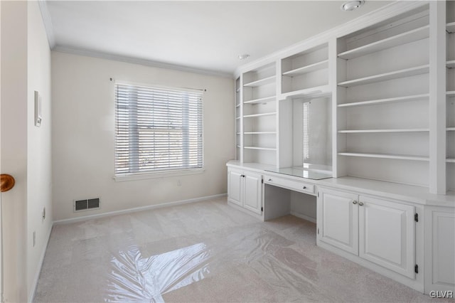 unfurnished office with visible vents, crown molding, baseboards, light colored carpet, and built in desk