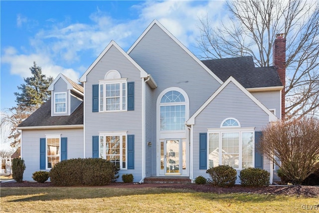 traditional-style home featuring a chimney, a front yard, and roof with shingles