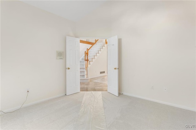 empty room with visible vents, baseboards, lofted ceiling, stairs, and light colored carpet