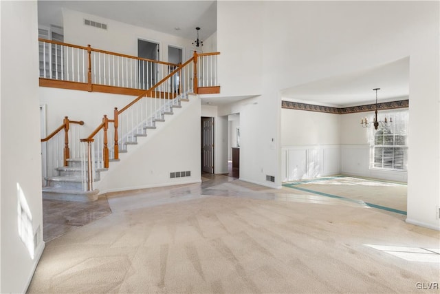 unfurnished living room featuring stairs, an inviting chandelier, carpet, and visible vents