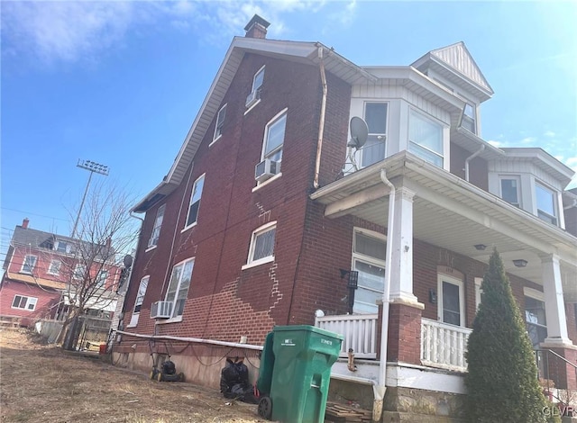 view of home's exterior featuring cooling unit, covered porch, brick siding, and a chimney