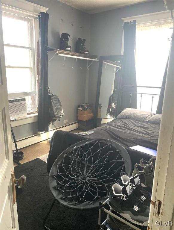 bedroom with a baseboard heating unit, multiple windows, and cooling unit