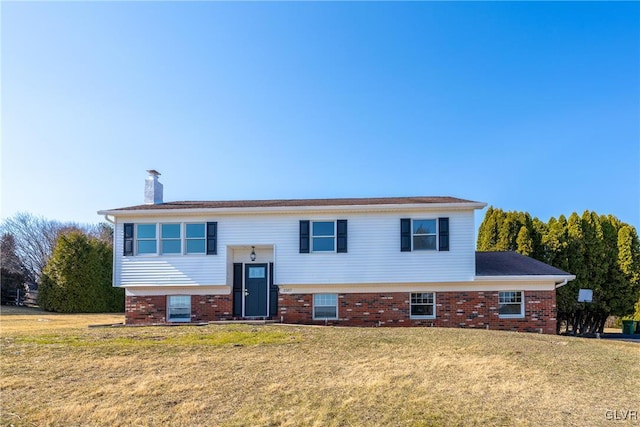 raised ranch featuring brick siding, a chimney, and a front yard