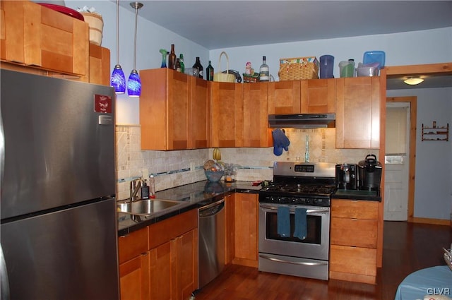 kitchen featuring a sink, stainless steel appliances, under cabinet range hood, dark countertops, and backsplash