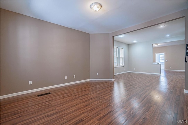 unfurnished room featuring dark wood finished floors, visible vents, and baseboards