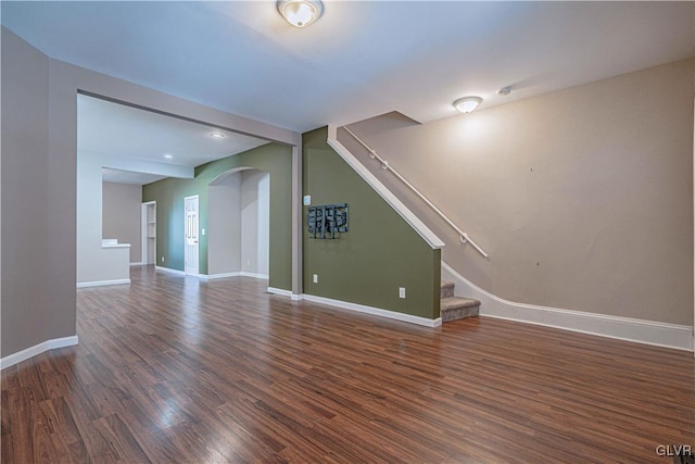 unfurnished living room featuring stairs, wood finished floors, baseboards, and arched walkways