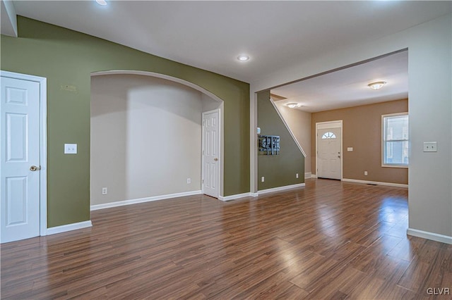 unfurnished room featuring baseboards, arched walkways, dark wood finished floors, and stairs