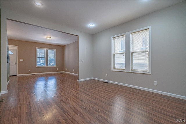 empty room with dark wood finished floors, visible vents, and baseboards