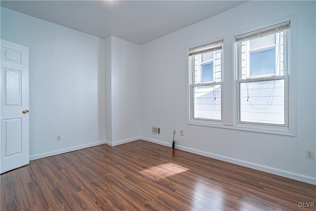 empty room featuring visible vents, dark wood-type flooring, and baseboards