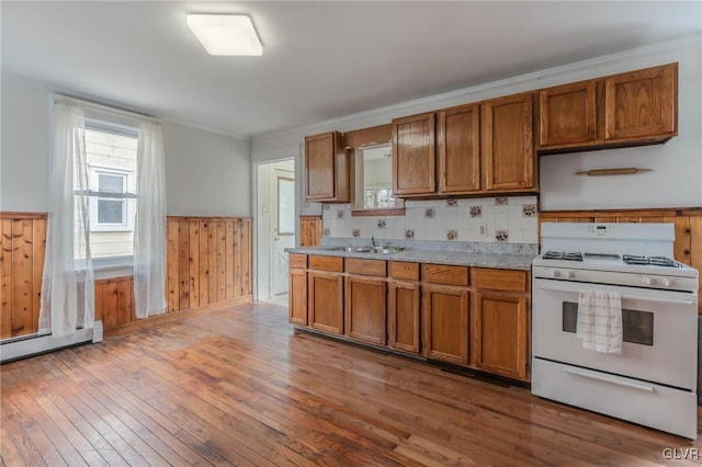 kitchen featuring brown cabinetry, wainscoting, white gas range oven, and light countertops