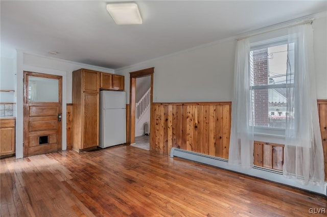 kitchen featuring brown cabinetry, a wainscoted wall, a baseboard radiator, freestanding refrigerator, and hardwood / wood-style flooring