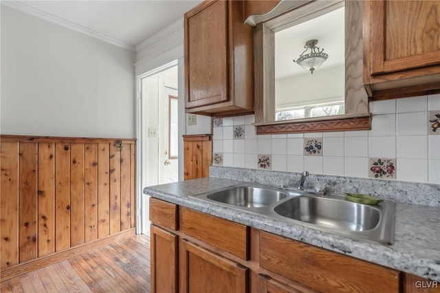 kitchen featuring light wood finished floors, crown molding, light countertops, brown cabinetry, and a sink