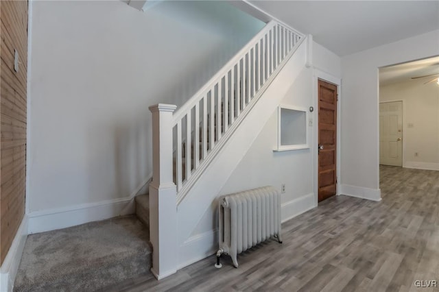 staircase with radiator heating unit, wood finished floors, and baseboards